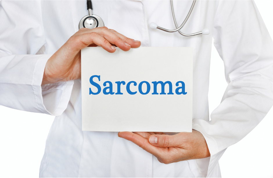 A photo of a person wearing a laboratory coat and a stethoscope holding a sign that says Sarcoma.